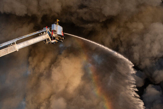 A rainbow forms in the spray as a firefighter douse a large indu