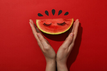 A slice of watermelon with decorative eyelashes on a red background