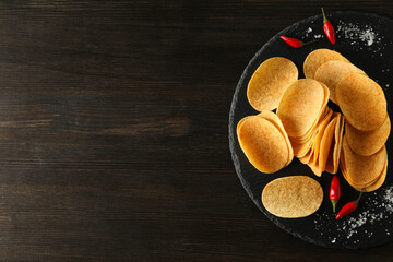 Potato chips in a bowl with chili peppers on a dark background