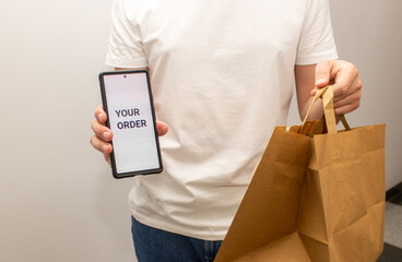 a courier  holds a package made of recycled craft paper and a phone with the inscription your...