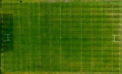Straight down aerial drone photo of a man cutting the grass of a British rugby pitch in the summer time showing the mower going down the sports field