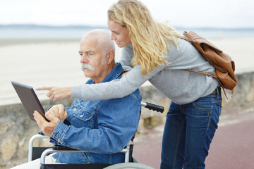 senior man in a wheelchair with tablet outdoors