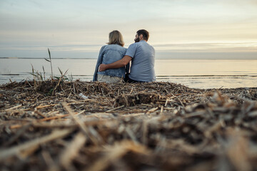 woman and man spending romantic time together on beach on sunset. View from behind