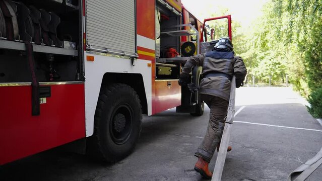 Young male fireguard with fire hose running to the place of emergency. Professional fireman in full equipment jogging to extinguishes fire. Concept of heroic profession and saving lives. Slow motion