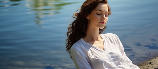 A teenage girl is peacefully relaxing by the water wearing a white shirt with plenty of copy space in the image