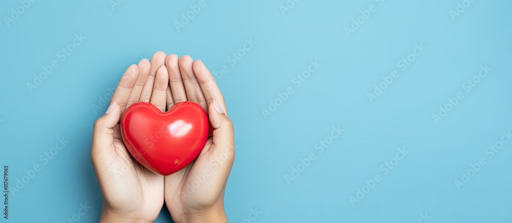 Poster a high angle image captures medical hands gently holding a heart on a light blue background offering