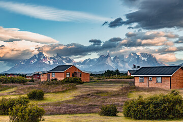 Wooden houses in the foreground of a mountain range under a cloudy sky at dawn