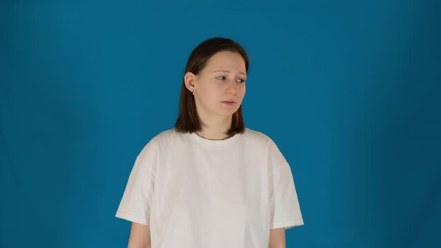 Young woman performs doubting on blue background. Female model with mistrust expression in studio. Confused lady poses for camera