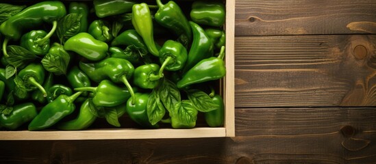 A top view of a delivery crate filled with fresh green peppers on light wooden panels with copy space provided