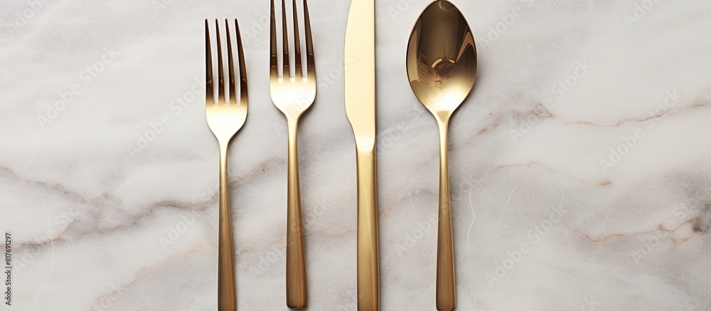 Poster design concept with clean golden metal cutlery on a light marble background in a top view copy space
