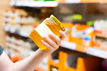 Young male hand holds honey on a blurred background, a row of shelves with groceries in supermarket