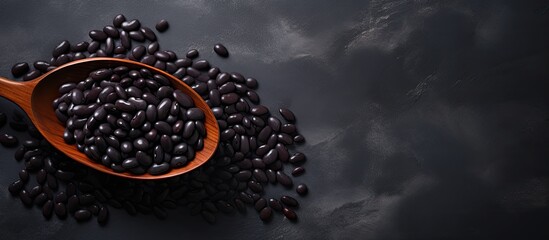 A copy space image of black beans in a ceramic bowl with a plastic spoon resting on a dark marble surface