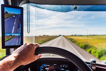 Hand holding the steering wheel of a truck with the view of a straight road out of focus on the...