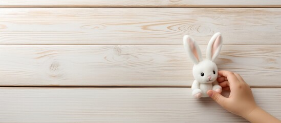 A baby s hand reaches out to touch a toy rabbit doll on an old white wooden table creating a charming copy space image - Powered by Adobe