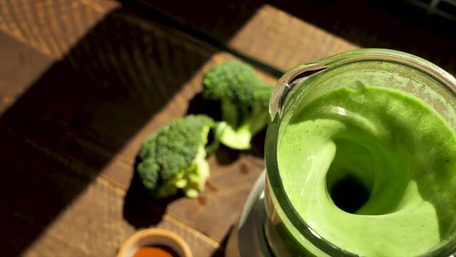 Top view: The camera moves over a blender in which a green diet smoothie is being blended in slow motion. Making a healthy green vegetable smoothie with broccoli, spinach, avocado and garlic