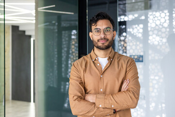 Confident young man with glasses standing and smiling in a modern office environment