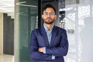 Confident business professional in blue suit standing with arms crossed in modern office