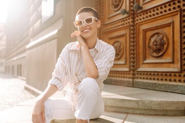 Fashionable young woman with a short haircut  in good mood posing sitting on the street stairs....