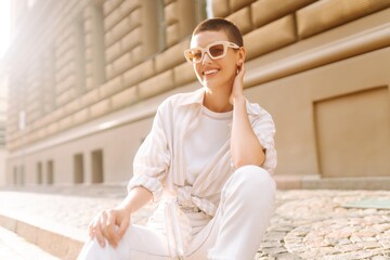 Fashionable young woman with a short haircut  in good mood posing sitting on the street stairs....