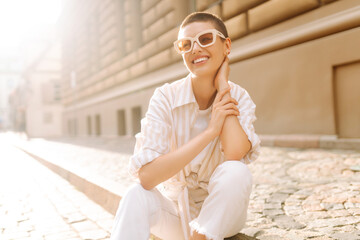 Fashionable young woman with a short haircut  in good mood posing sitting on the street stairs....