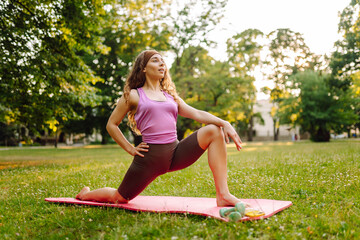 Young woman in sportswear stretching body on fitness mat at public park, doing yoga. Healthy lifestyle, sport. Fitness. Woman doing yoga in morning park.