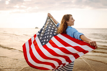 Young woman holding national American flag cover ocean beach holiday travel at summer romantic sunset. America independence day concept. 4th of July.
