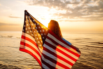 Young woman holding national American flag cover ocean beach holiday travel at summer romantic sunset. America independence day concept. 4th of July.