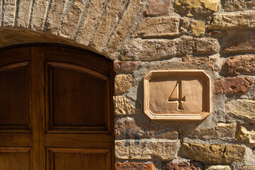 Wooden rectangle sign with the number four in classic brown font, hanging on brick facade of...