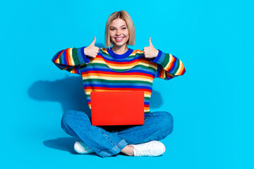 Full size photo of pretty young girl sit floor netbook thumb up wear trendy striped outfit isolated on blue color background