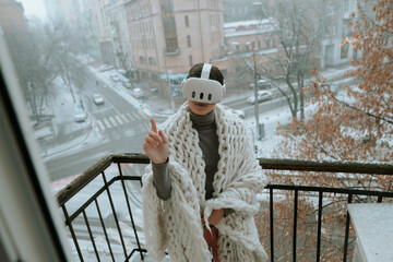 On the balcony in winter, a girl embraces virtual reality adventures with a headset.
