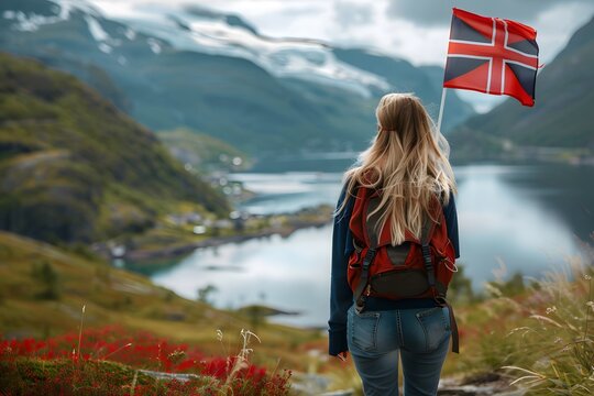 Blond woman with a norwegian flag admiring lake and mountains