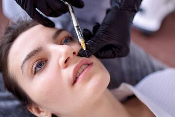 Beauty injections. Female cosmetologist in black gloves makes an injection