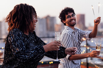 Glamorous African girls in elegant dresses and mixed-race smiling man drink champagne