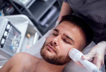Fototapeta premium Closeup of face of beautiful relaxing man undergoing hardware cosmetology procedure in spa