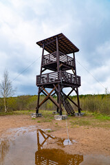 Beautiful image of a birdwatching tower reflecting in a puddle, set against a backdrop of cloudy...