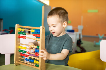 Smiling toddler boy playing with colourful toy abacus in a children's entertainment center....