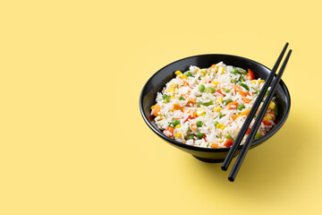 White rice with vegetables in a black bowl on yellow background. Copy space
