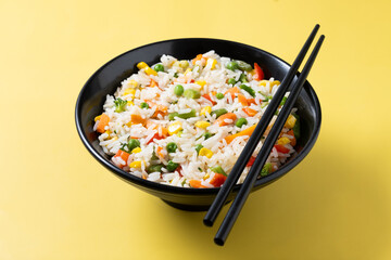 White rice with vegetables in a black bowl on yellow background