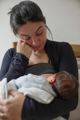 Weary mother breastfeeding her newborn, tears in her eyes, embodying the emotional and physical...