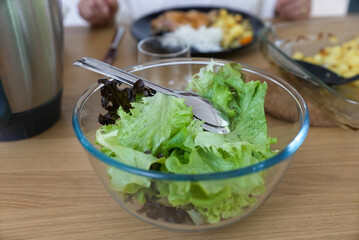 Fresh green salad in a glass bowl with a stainless steel serving spoon on a wooden table. The...