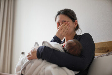 Mother breastfeeding her newborn baby while covering her face with her hand, indicating tiredness...