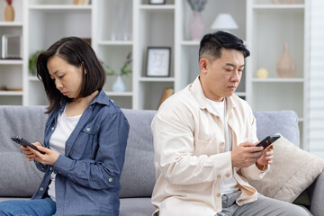 Couple sitting apart on a sofa, focusing on their smartphones. Concept of technology affecting...