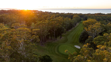 Obraz premium a bird's eye view of a golf course with the sun rising over trees