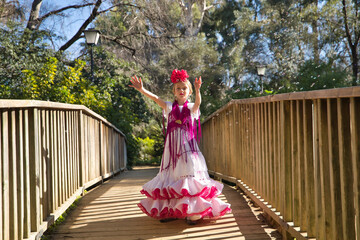 A girl dancing flamenco, playing with soap bubbles, in typical flamenco dress, on a wooden bridge....