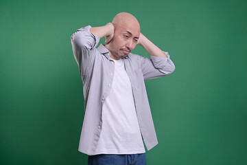 Bald man covering ears with hands isolated on green background.