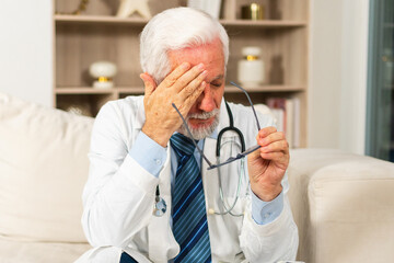 Sad tired mature senior male doctor in medical uniform in hospital or doctor office. Unhappy...
