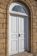 Fototapeta premium The vaulted entrance to the house. White wooden door. The masonry walls of the house are made of natural stone. Environmentally friendly building material. The shell rock.