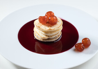 Stack of pancakes topped with fresh red berries arranged on a white plate