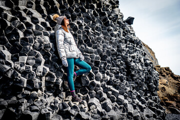Woman in silver coat and beanie next to basalt formations in Reynisfjara in Iceland