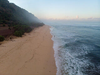A lone figure walks on a misty beach beside the gentle waves at dawn